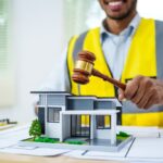 Man holding gavel, looking at model house. Contractor’s Registration impact on Construction Liens in Real Property Development