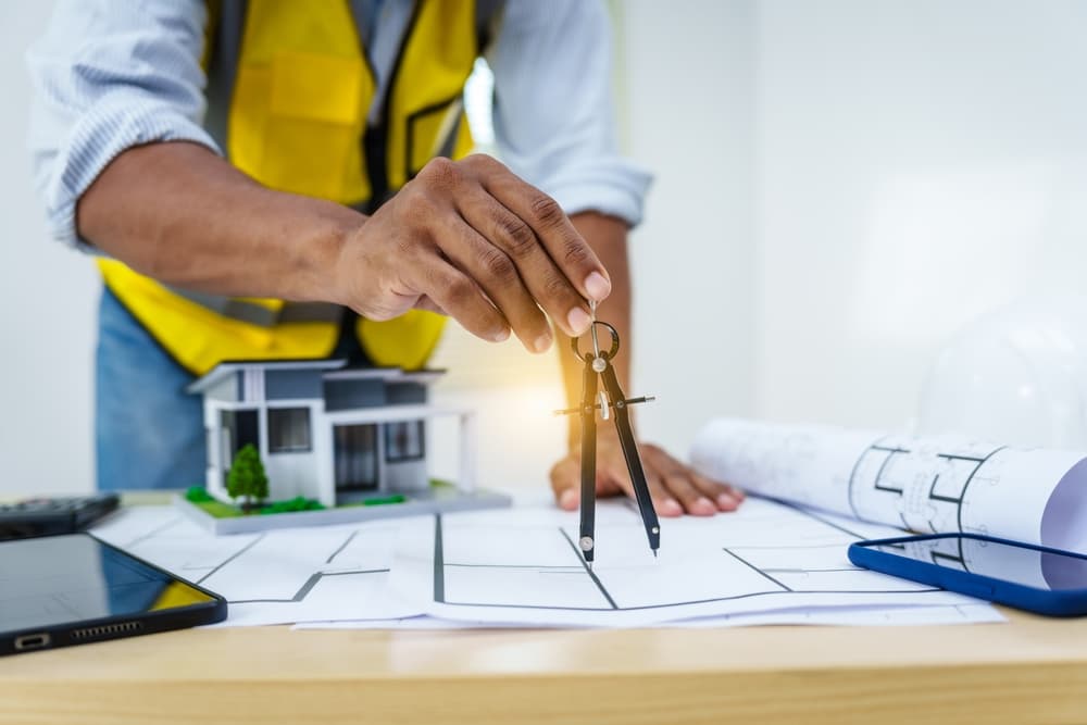 A male architect works at desk with house model toy and A3 paper blueprints, construction real estate law, zoning, permits, and resolving property disputes through arbitration and litigation.