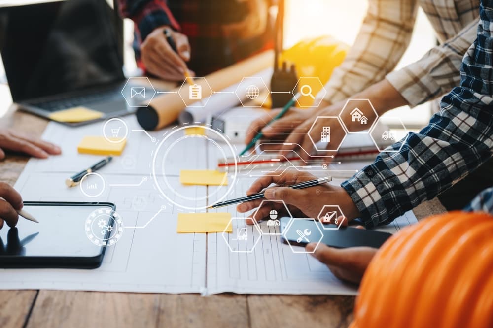 Engineers collaborate on blueprints and project models during a teamwork meeting in an office setting. The team, including Asian industry professionals, works together on building plans.