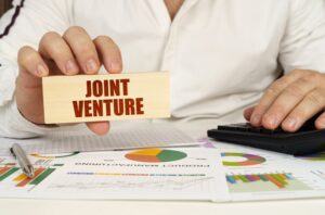 On the table are business charts and diagrams in the hands of a wooden block with the inscription - Joint Venture