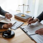 Lawyer and businessman reviewing contract details together, discussing business agreements and financial investments, with legal books and documents on the desk.