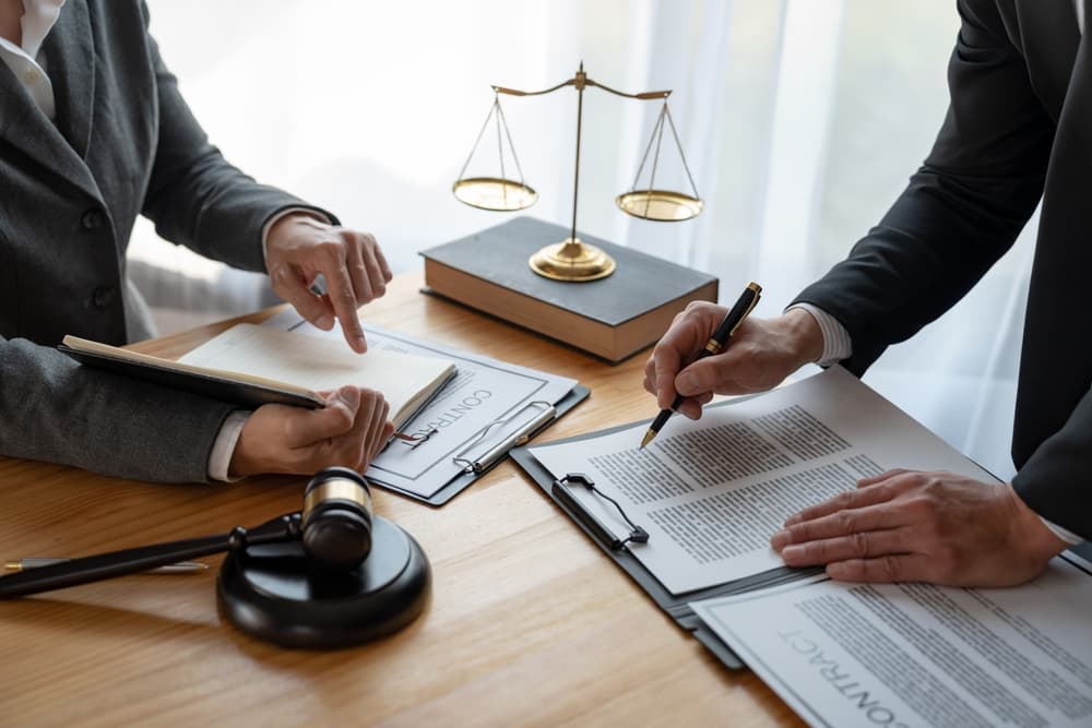 Lawyer and businessman reviewing contract details together, discussing business agreements and financial investments, with legal books and documents on the desk.