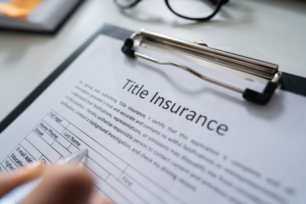 Close-up of a woman filling out a title insurance form on a white desk, with a pen and documents visible