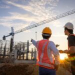 A team of construction engineers talks to managers and construction workers at the construction site.